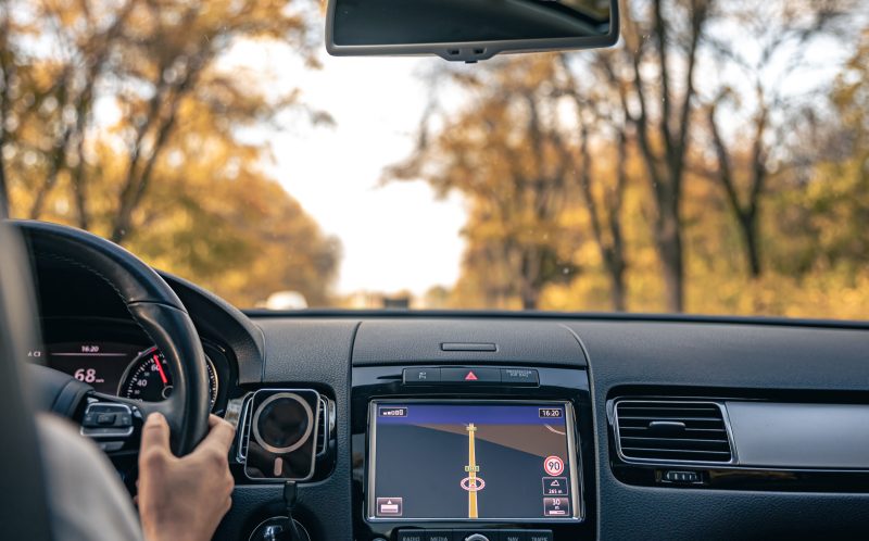 A close-up view of a Mazda Connect infotainment system screen displaying a navigation map, with a hand inserting or removing an SD card from its slot, illustrating the process of managing map data for in-car navigation.