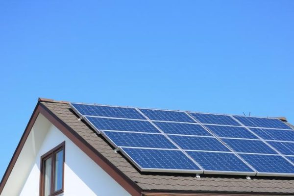 saulės baterijos ant namo stogo saulėtą dieną, simbolizuojančios elektros sąskaitų mažinimą